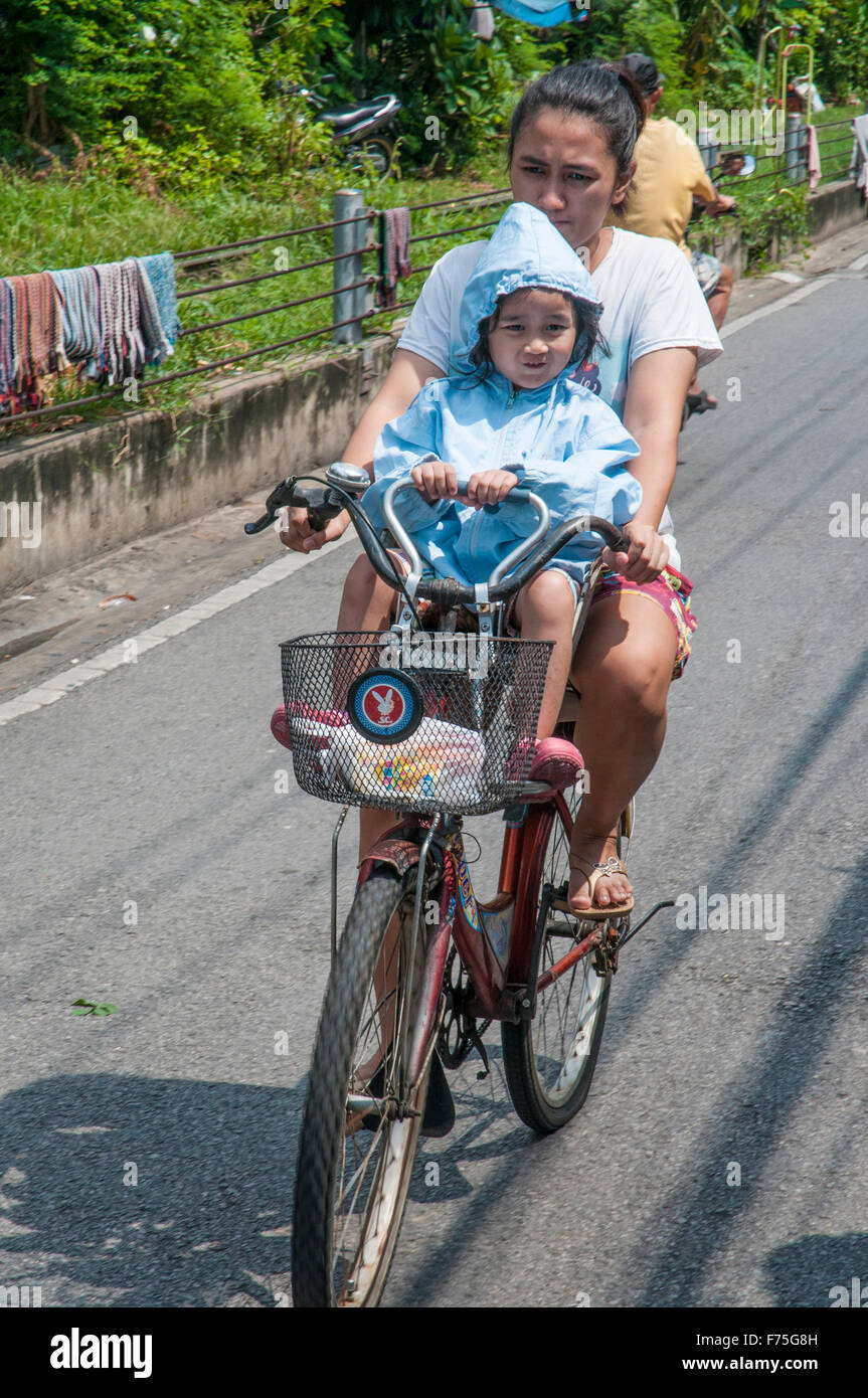 Infant riding bicycle with its mother in a residential district of Dhonburi, Bangkok, Thailand Stock Photo