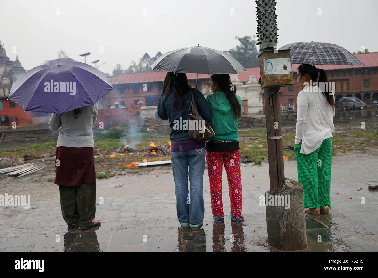 Women watching cremation with umbrellas in rain, earthquake deaths, kathmandu, nepal, asia Stock Photo