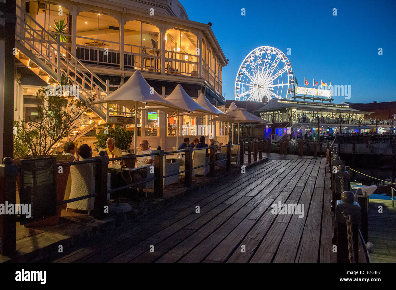 People eating at a restaurant outdoors in the evening at the V and A Waterfront , downtown Cape