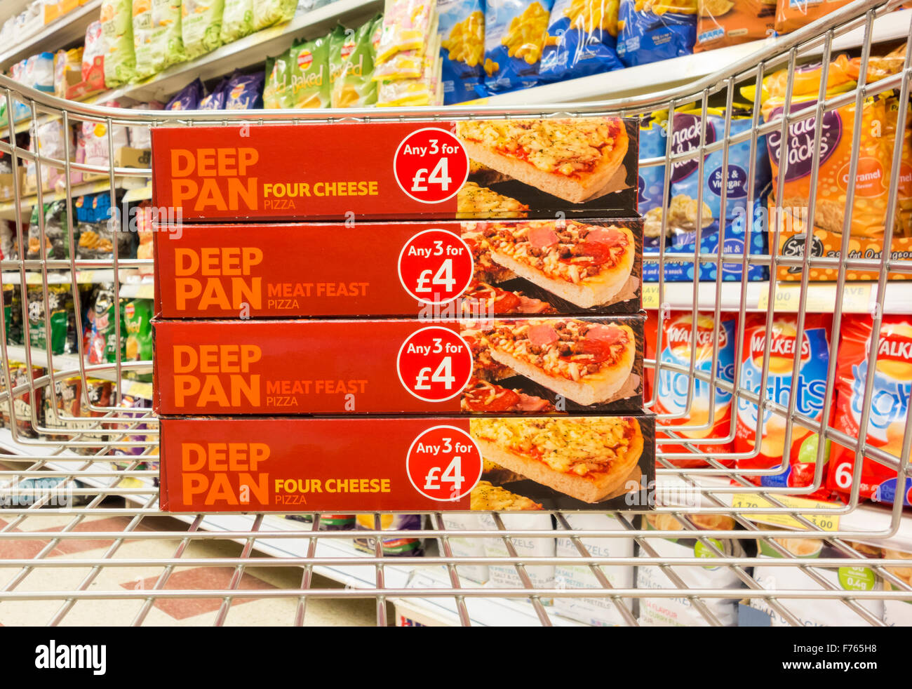 Four Tesco Deep Pan Pizzas in shopping trolley with crisps in background. Healthy/unhealthy diet concept... Tesco store, UK Stock Photo