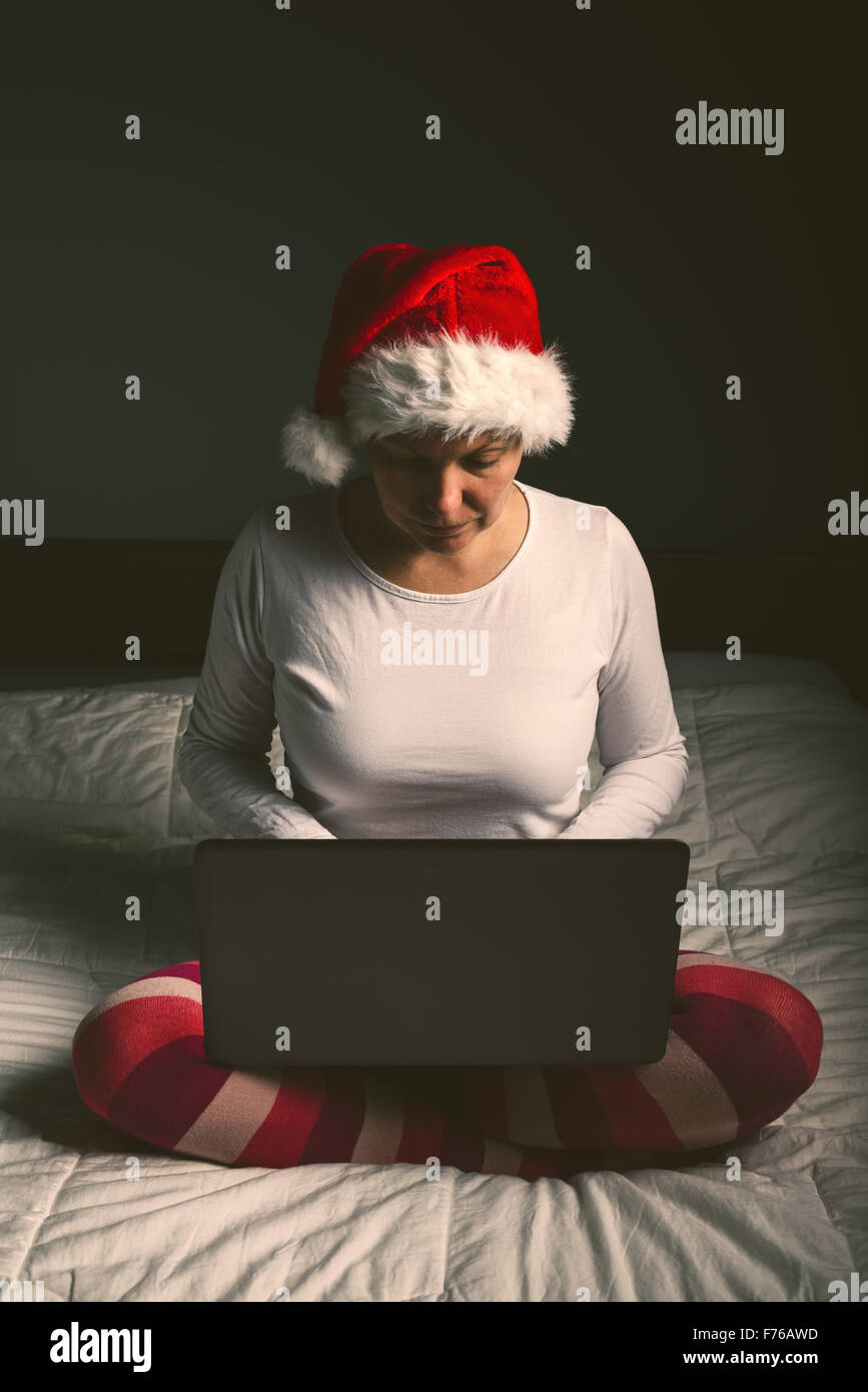 Lonely woman browsing internet on Christmas eve, adult female using laptop computer to access social network sites, retro toned Stock Photo
