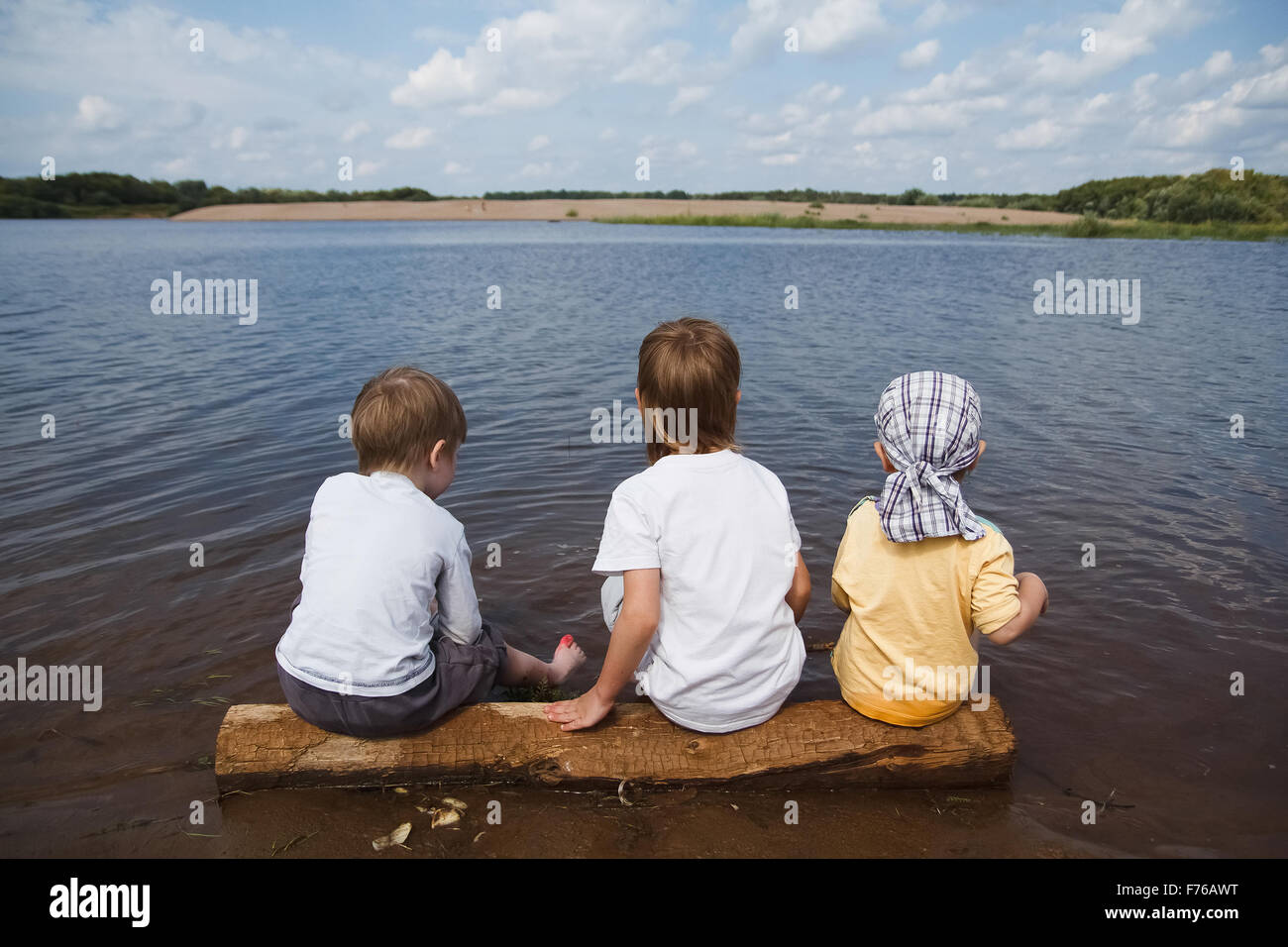 three boys sitting on the Bank of the lake Stock Photo