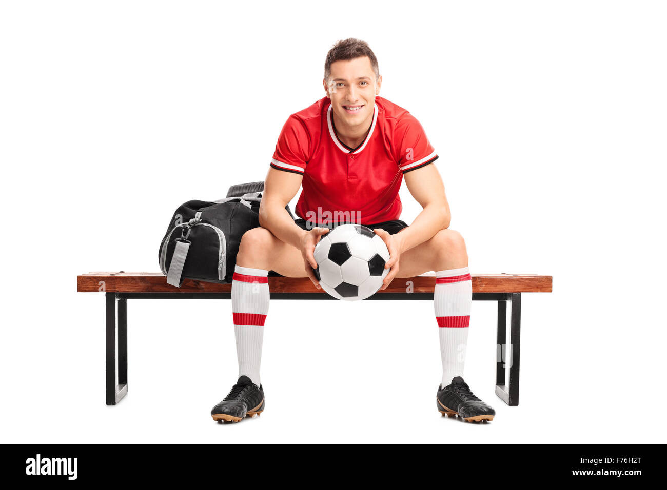 Young football player holding a ball and sitting on a wooden bench isolated on white background Stock Photo