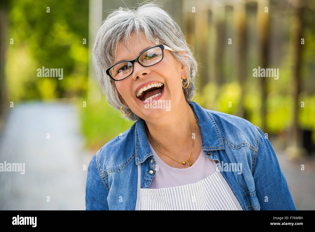 Beautiful mature woman working in a greenhouse, looking at camera while laughing Stock Photo