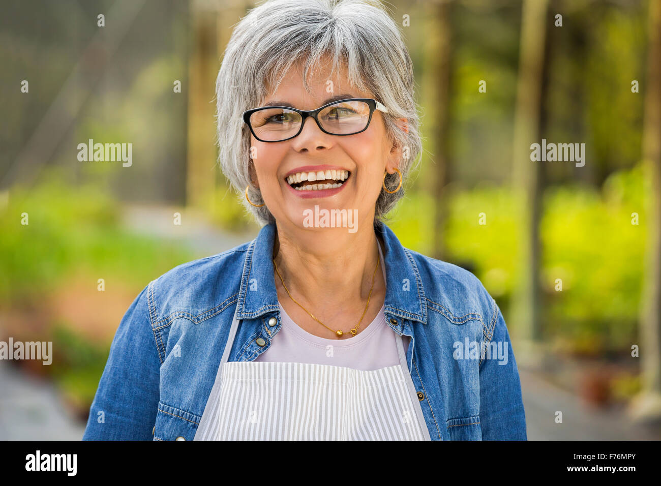 Beautiful mature woman working in a greenhouse, looking at camera while laughing Stock Photo