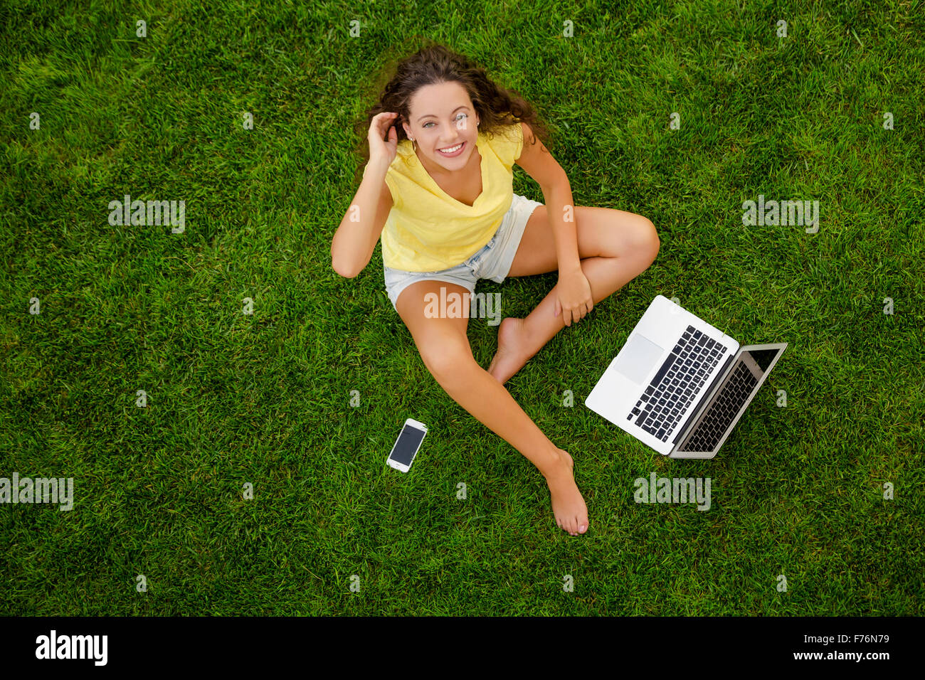 Beautiful young woman sitting on the grass and working with a laptop ...