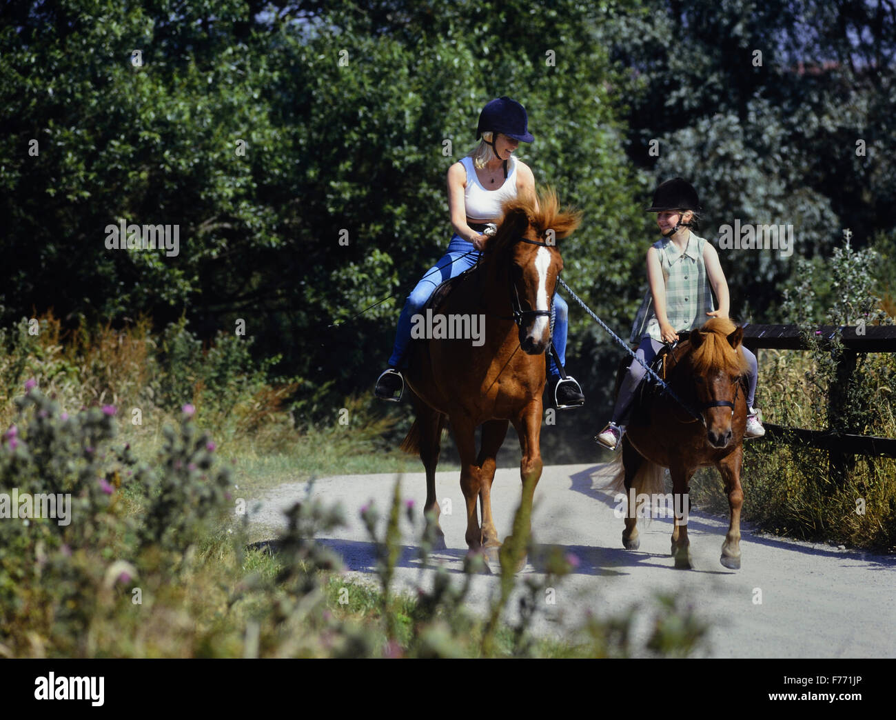 Mother and daughter riding together using a lead rein to train a pony and young horse rider. UK