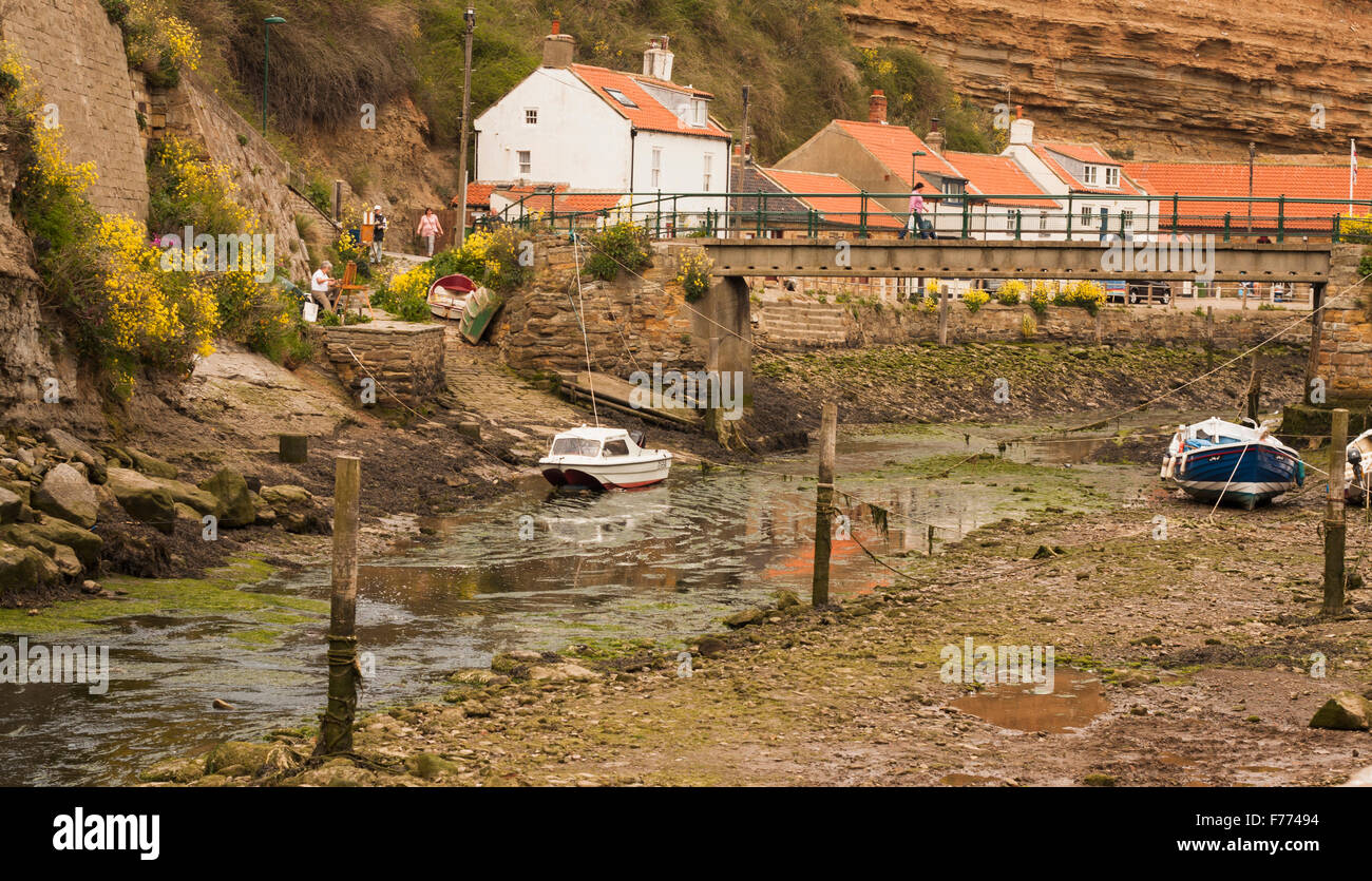 Picturesque view of Staithes fishing village,North Yorks showing artists at work,moored boats,footbridge and houses Stock Photo