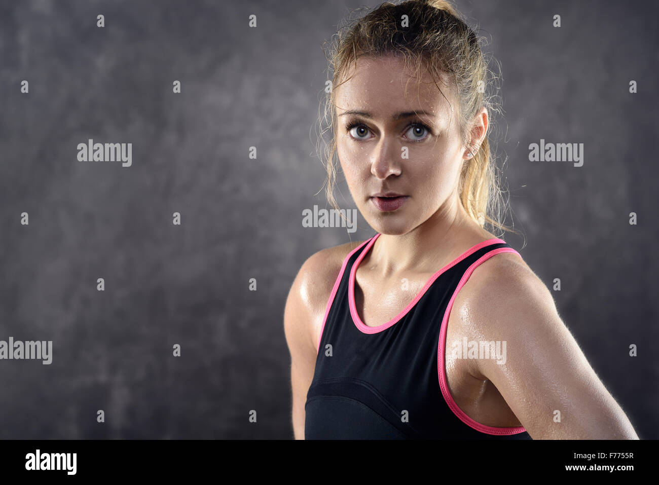 Head and Shoulders Portrait of a sweating Athletic Blond Woman Wearing Pink and Black Tank Top and Standing with Hands on Hips i Stock Photo