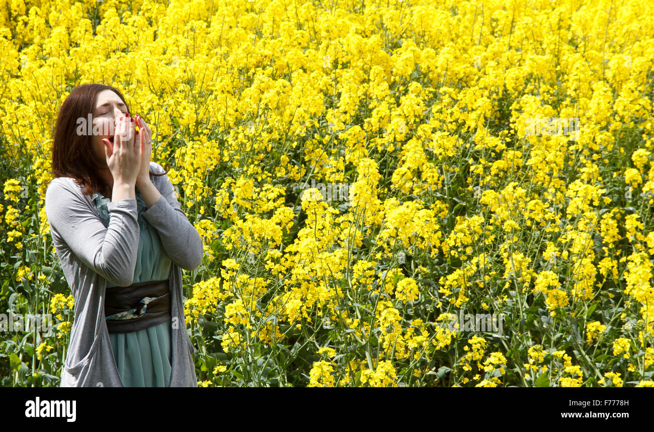 Female sneezing with hayfever in bright yellow rape seed field Stock Photo