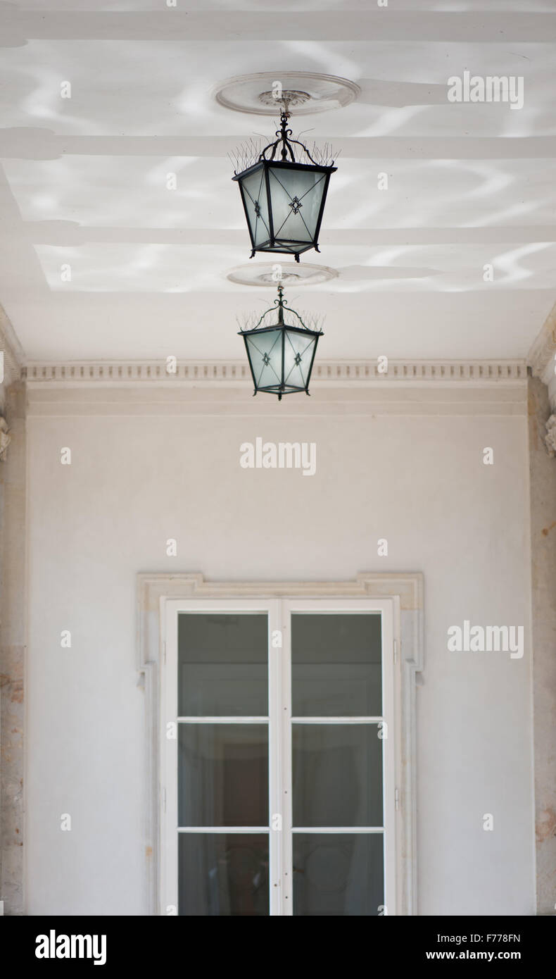 Hanging decorative two lamps under ceiling near window, ornamental outside lanterns architecture detail with bird spikes... Stock Photo