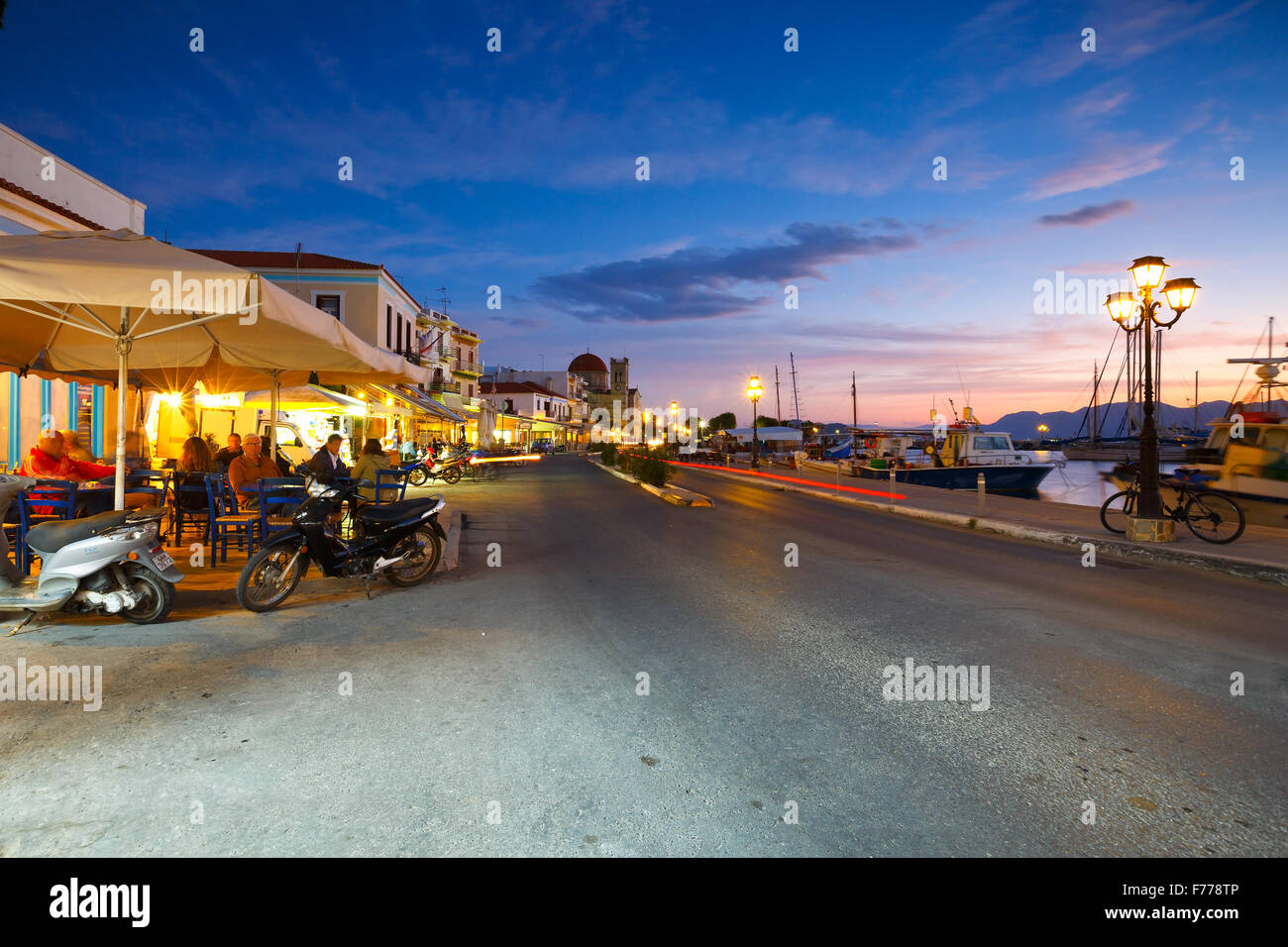 View of the seafront with coffee shops, bars and restaurants and fishing boats in the harbour of Aegina island, Greece Stock Photo