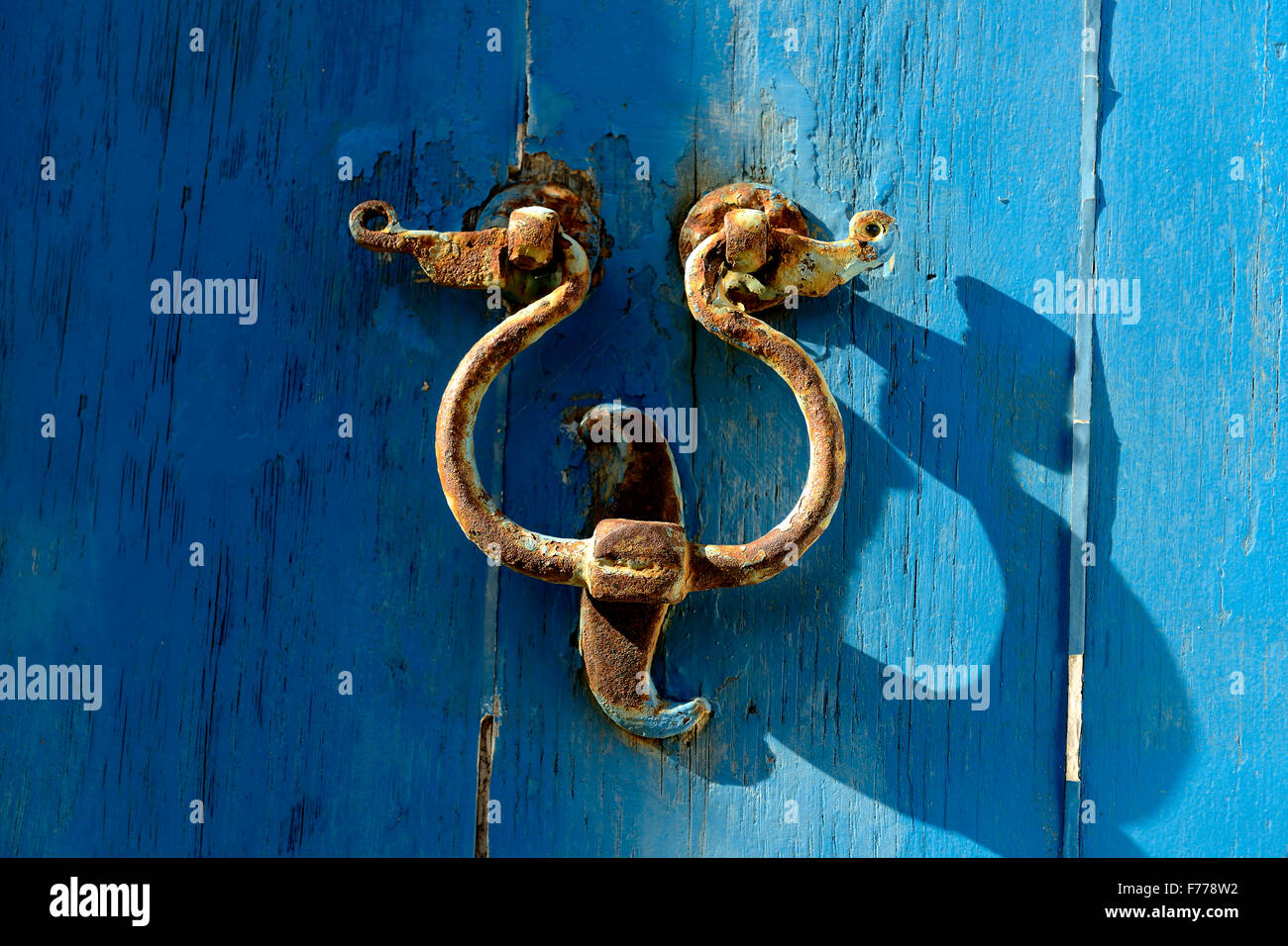 Old door knocker on the door with a blue background. A metal instrument to a hinged door and rapped by visitors to attract atten Stock Photo