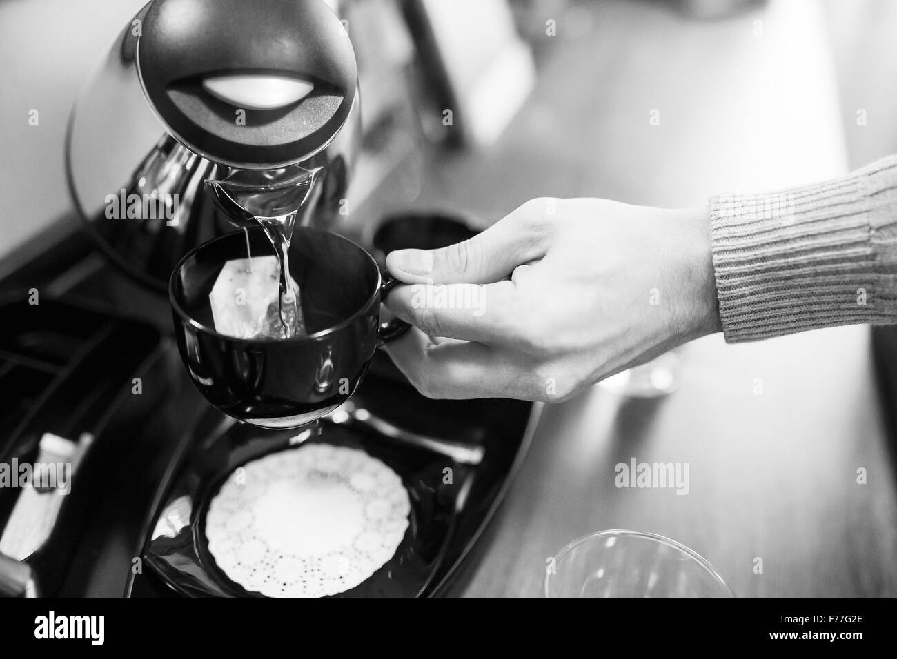A man pours tea from a kettle into a mug in the kitchen. Stock Photo