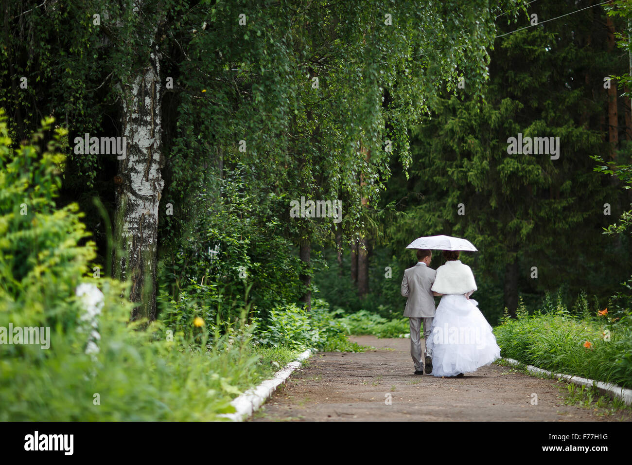 Beautiful just married couple under umbrella walking away on road