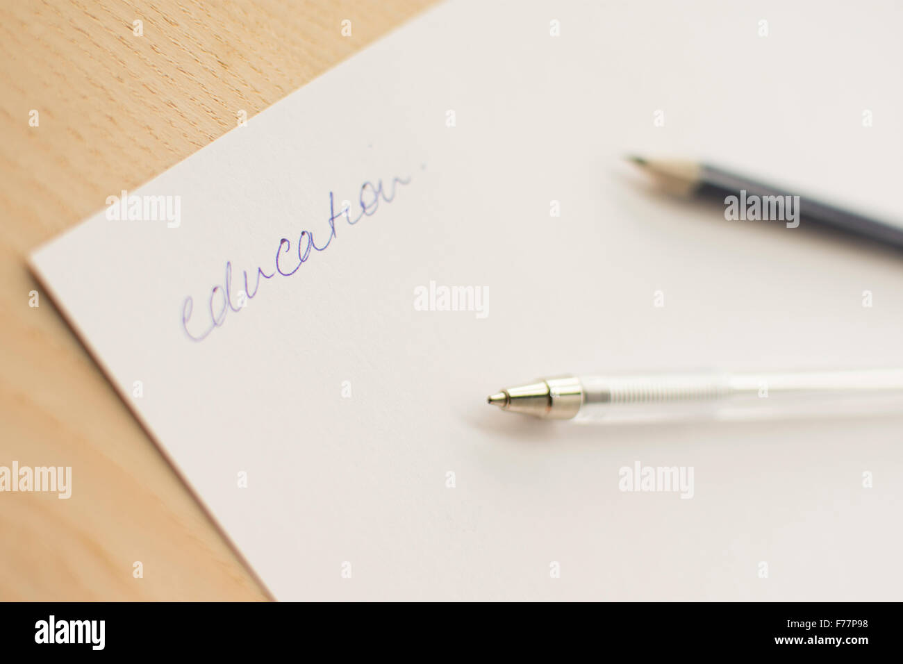 The word 'education' in blue pen on white paper laid out on a wooden board or table top. Stock Photo