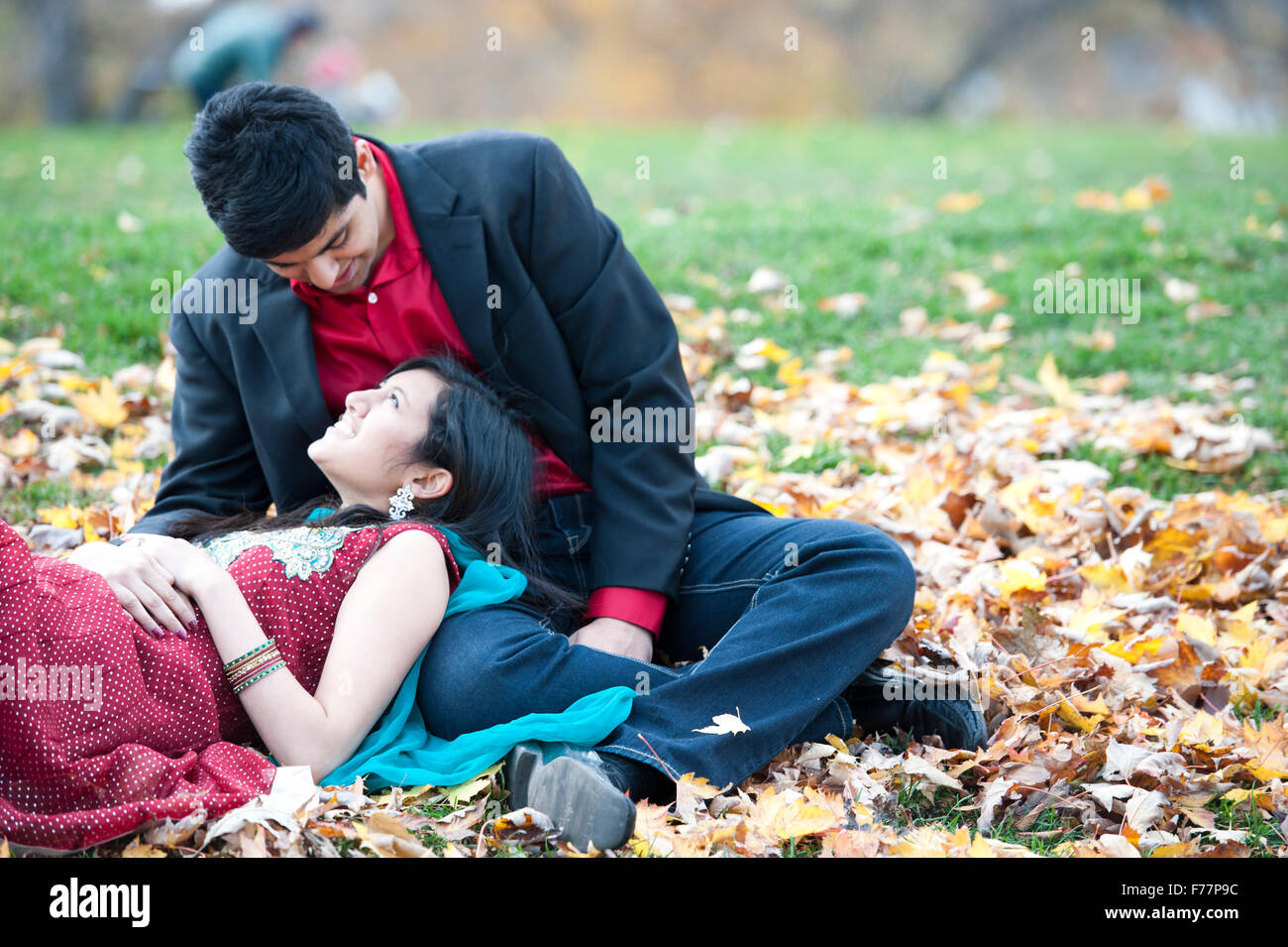 A young and happy Indian couple posing on a pile of leaves in the fall ...