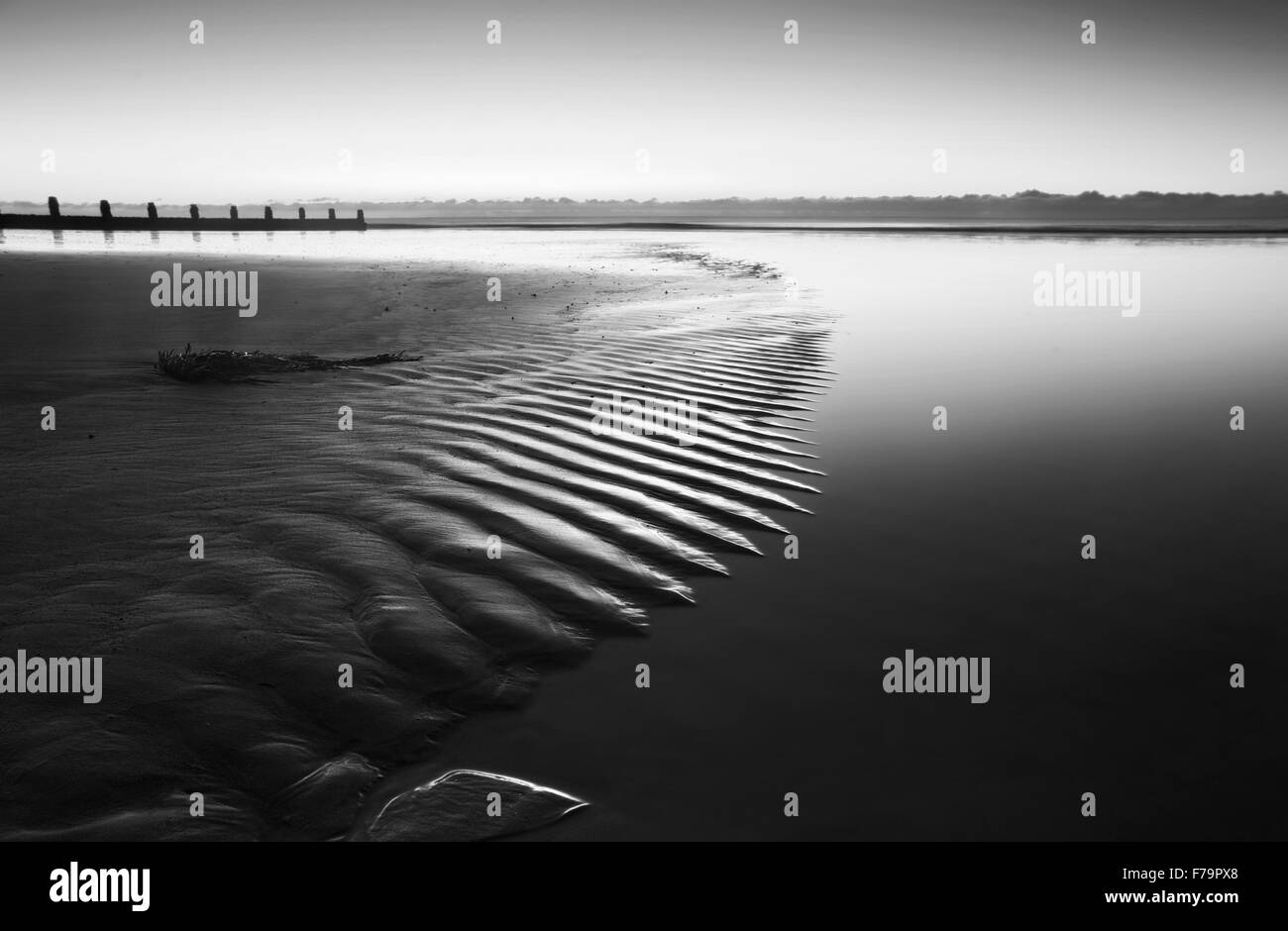 Beautiful low point of view along beach at low tide out to sea with vibrant sunrise sky in black and white Stock Photo