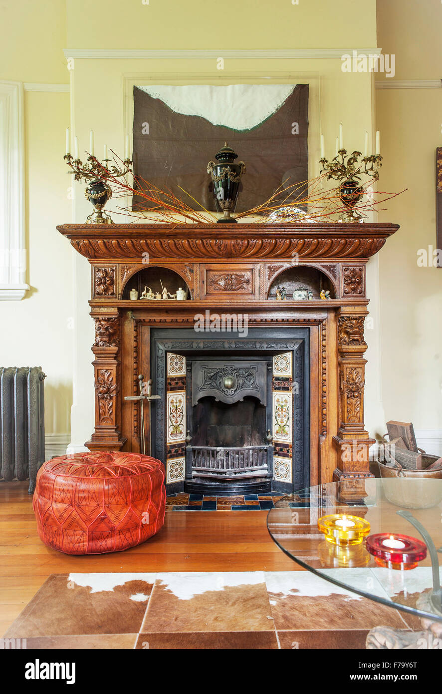 Leather pouf by a carved wooden fireplace in home of designer Erica Pols, Australia. An animal skin on the wooden floor. Stock Photo