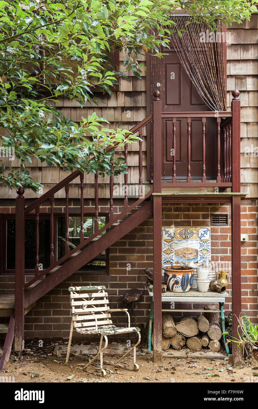 Garden flat exterior, home of designer Erica Pols. The steps up to the door. A log store and garden chair. Stock Photo