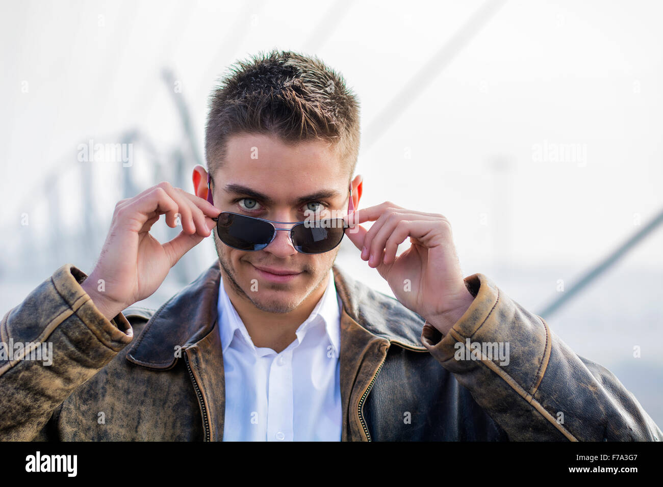 Handsome trendy young man standing on a sidewalk wearing sunglasses and ...