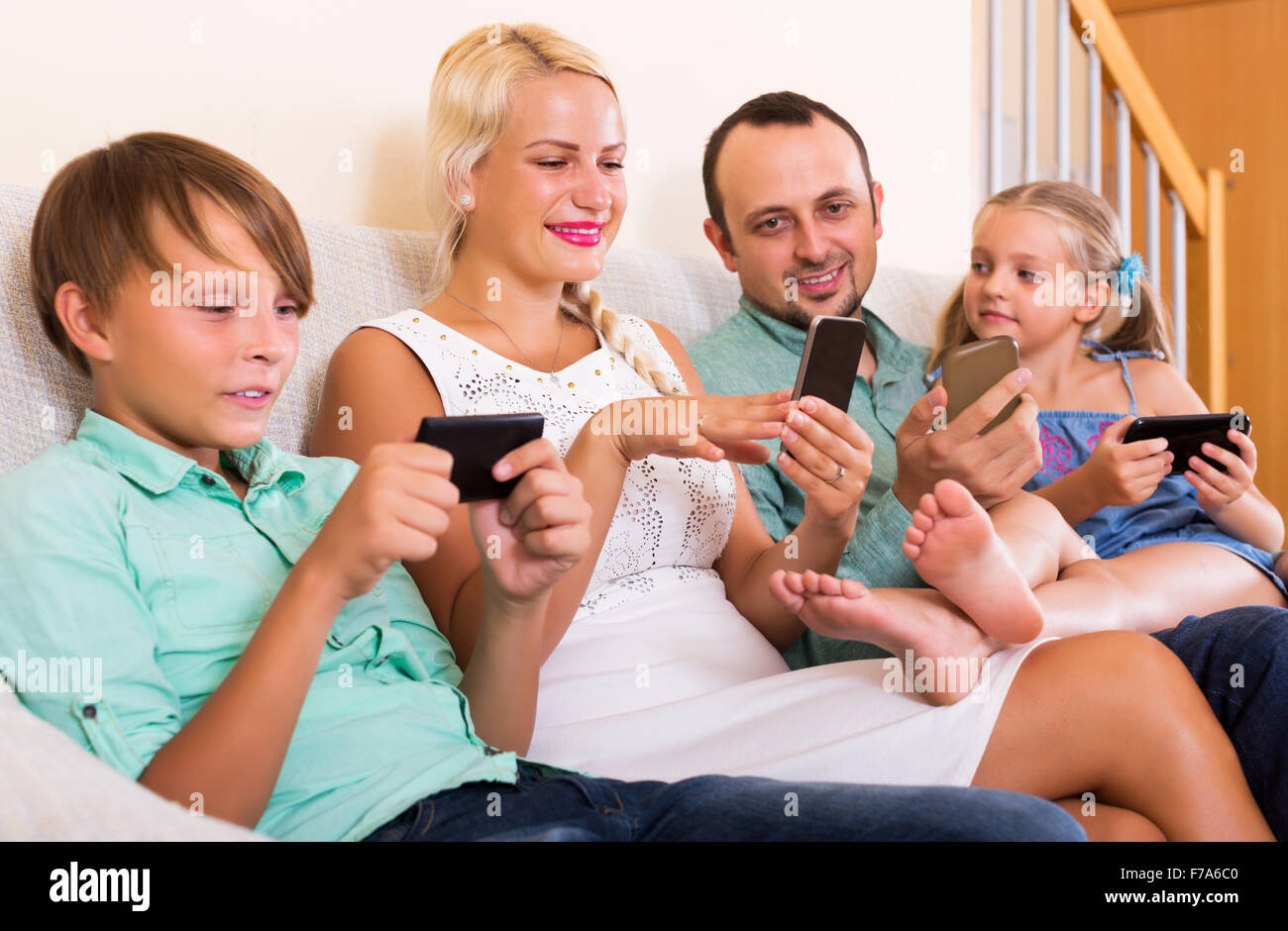 Young mom, dad and two happy kids working with smartphones indoors ...