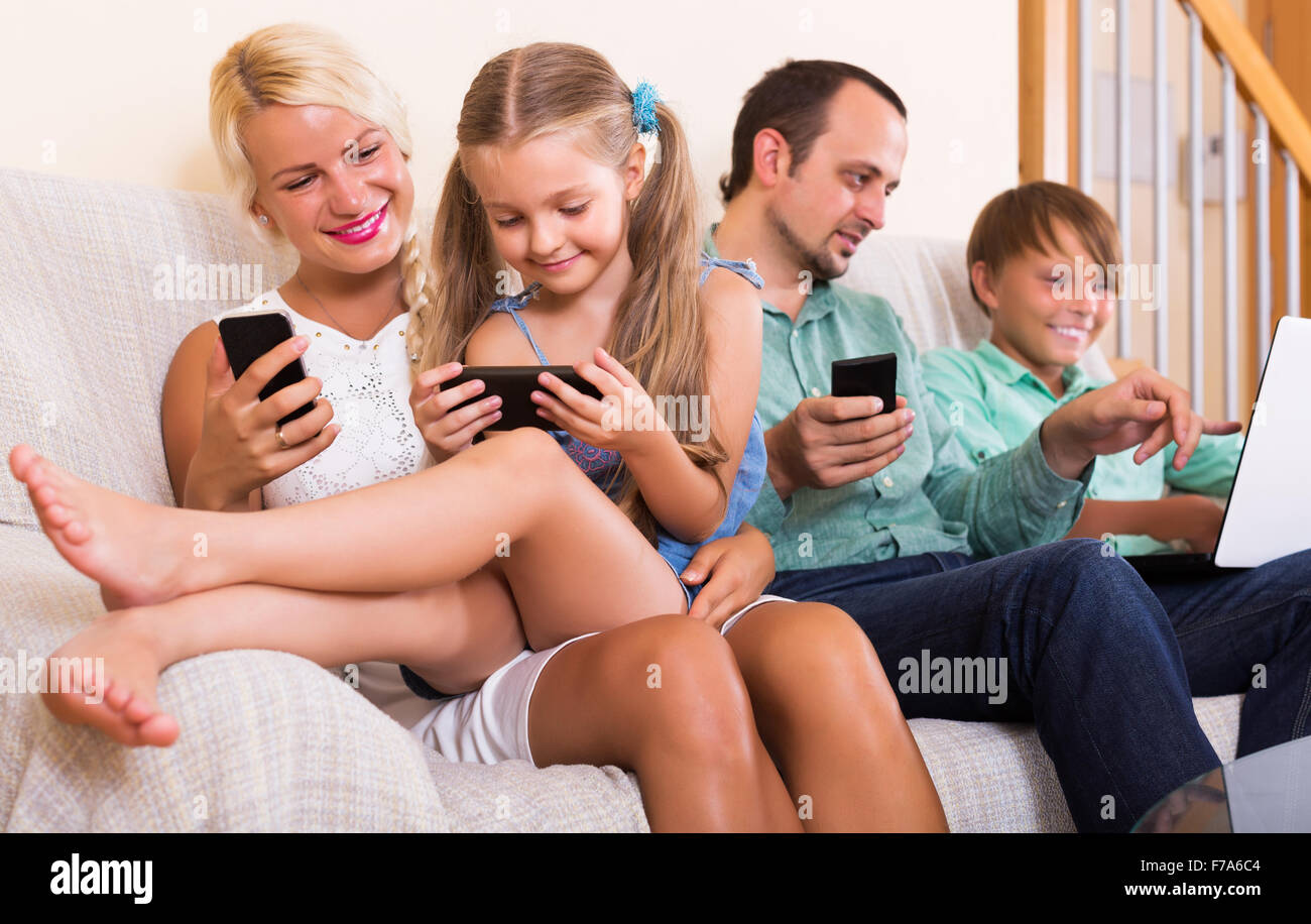 Happy young mom, dad and two kids working with smartphones indoors ...