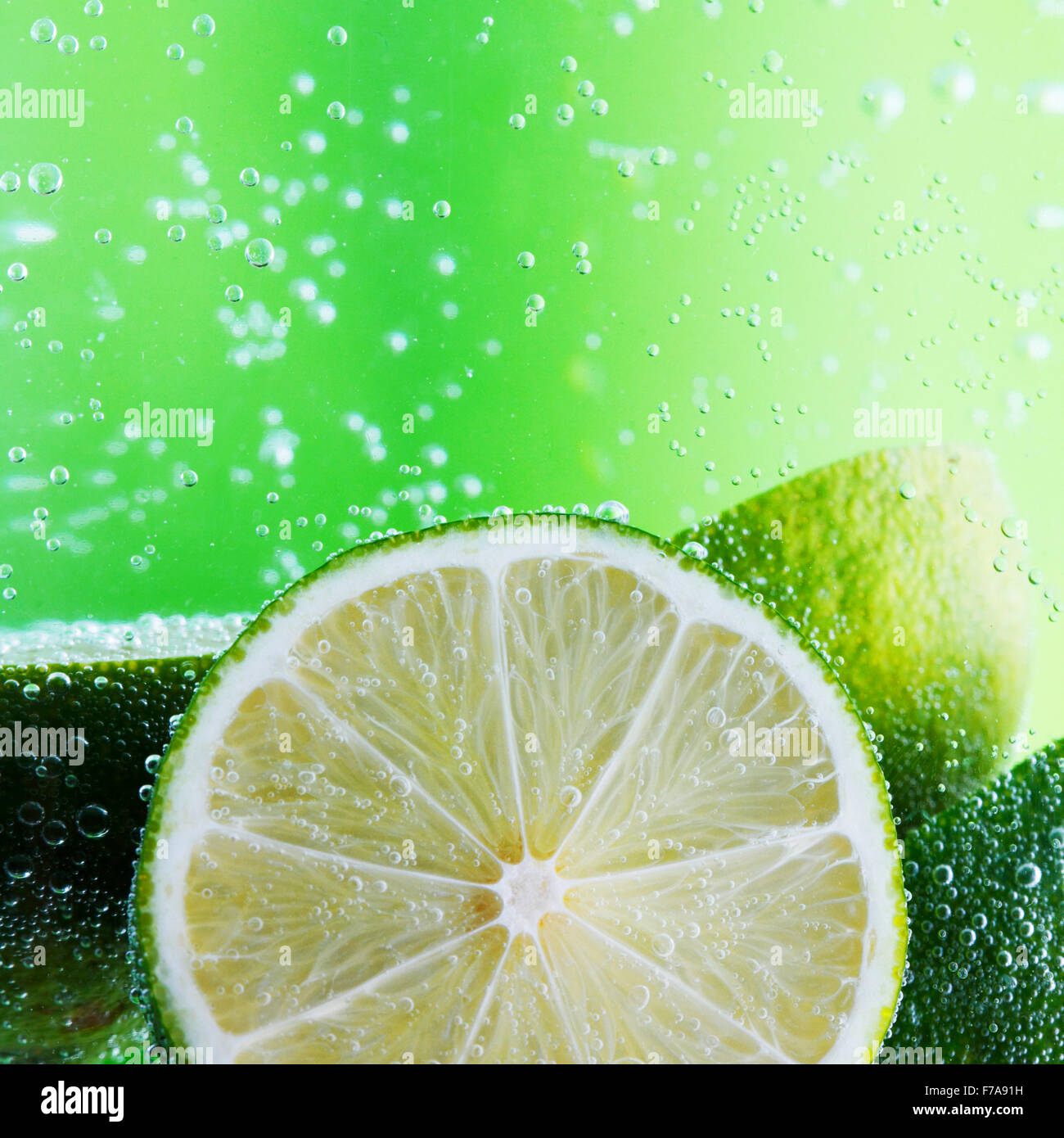 Cut limes in the water with bubbles on green background Stock Photo