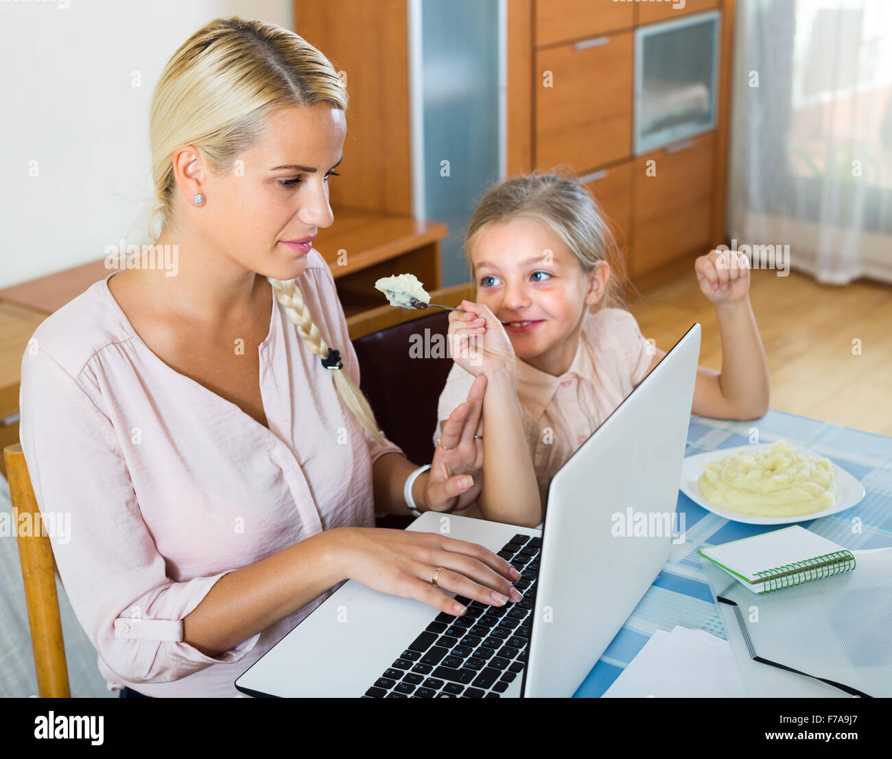 Tired businesswoman irritated as little daughter diverts her from laptop at home Stock Photo