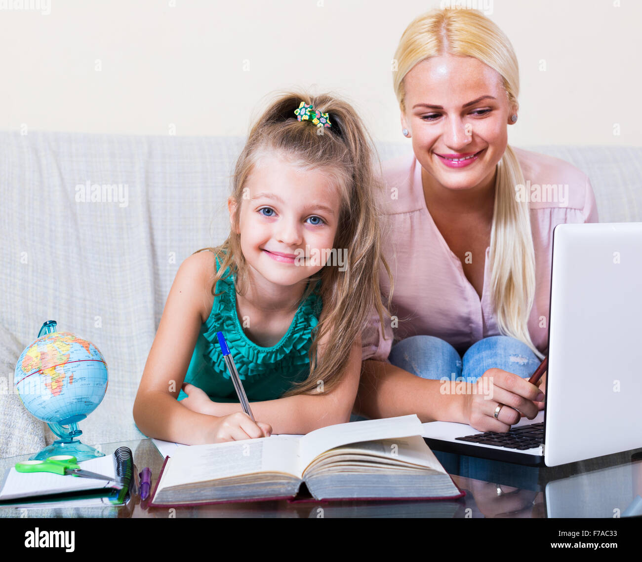 Portrait of positive adult woman and her child having lesson indoors ...