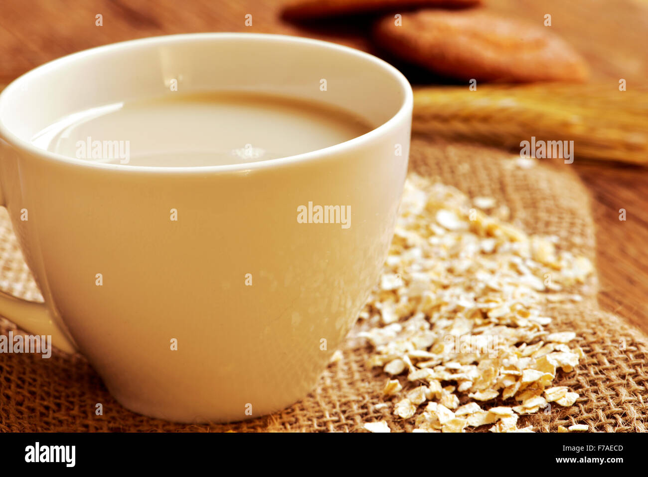 closeup of a cup with oat milk and some rolled oats on a rustic wooden table, and some digestive cookies in the background Stock Photo