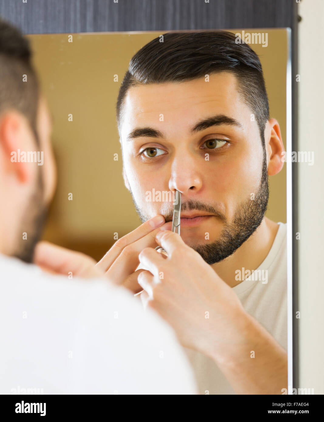Man Looking At Mirror And Removing Nose Hair With Tweezers Stock