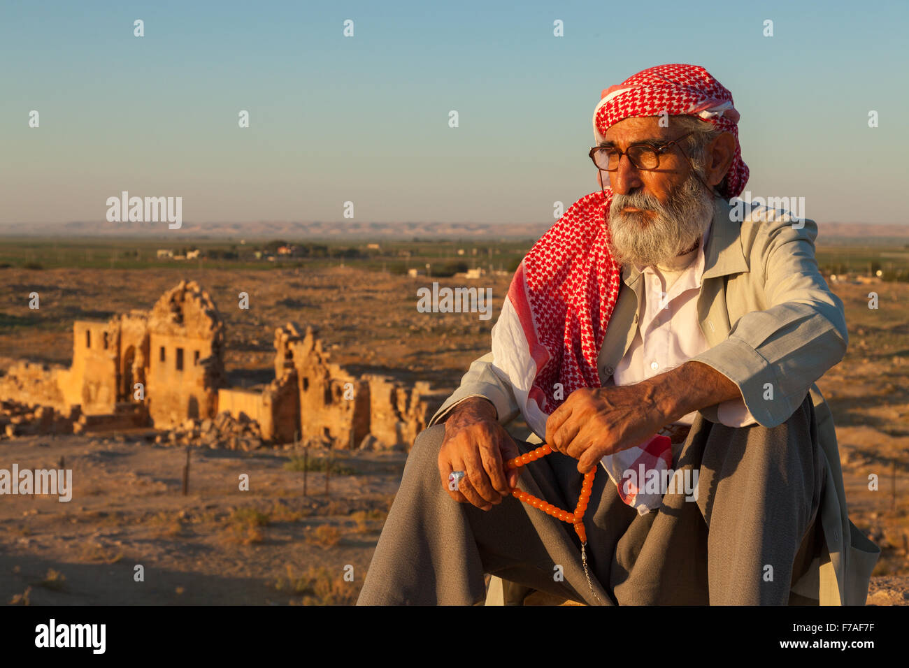 Unidentified man keeping prayers bead in hand sits in front of the ruins of ancient Harran University and Ulu cami (Ulu mosque), Stock Photo