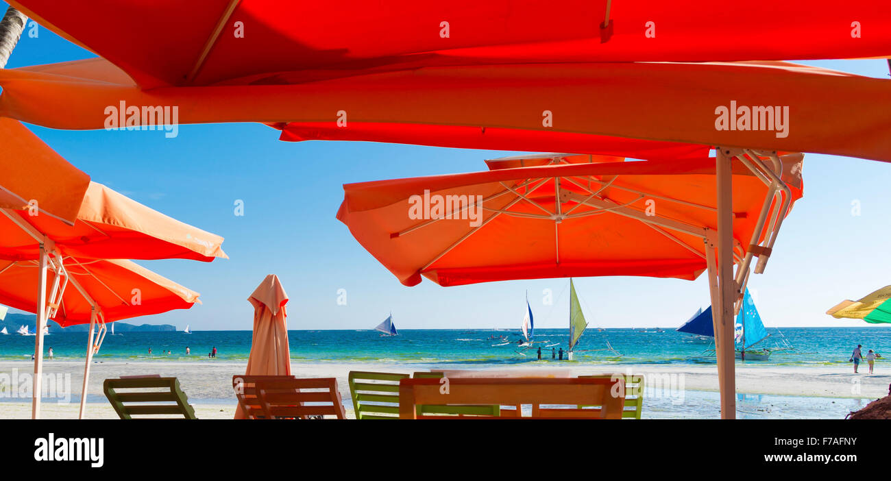 tropical beach with chairs covered by orange umbrellas Stock Photo