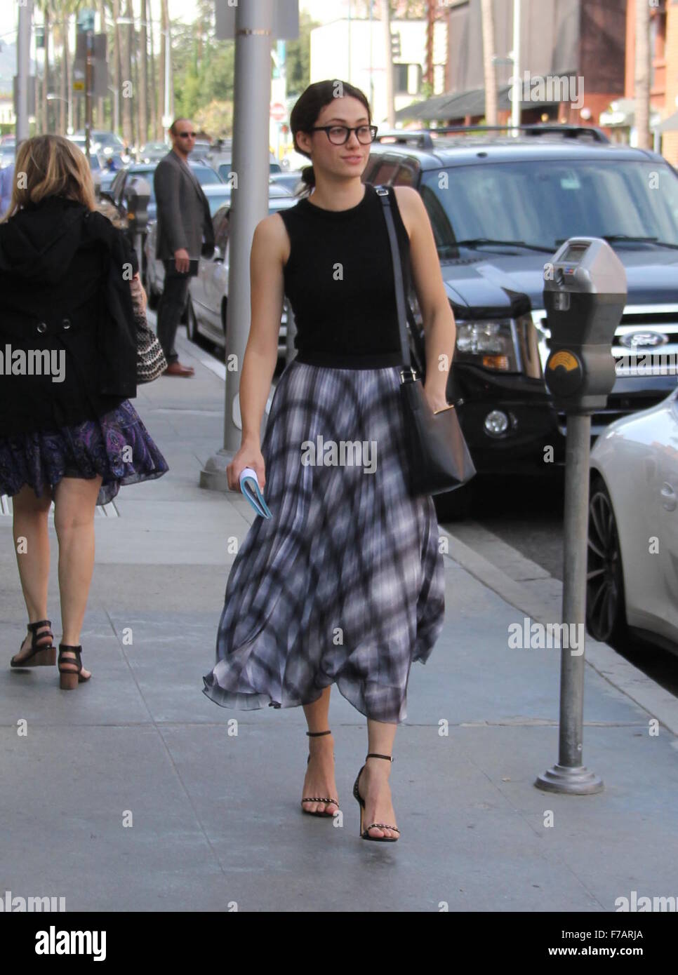 Emmy Rossum wears a flowy plaid skirt and black framed glasses while
