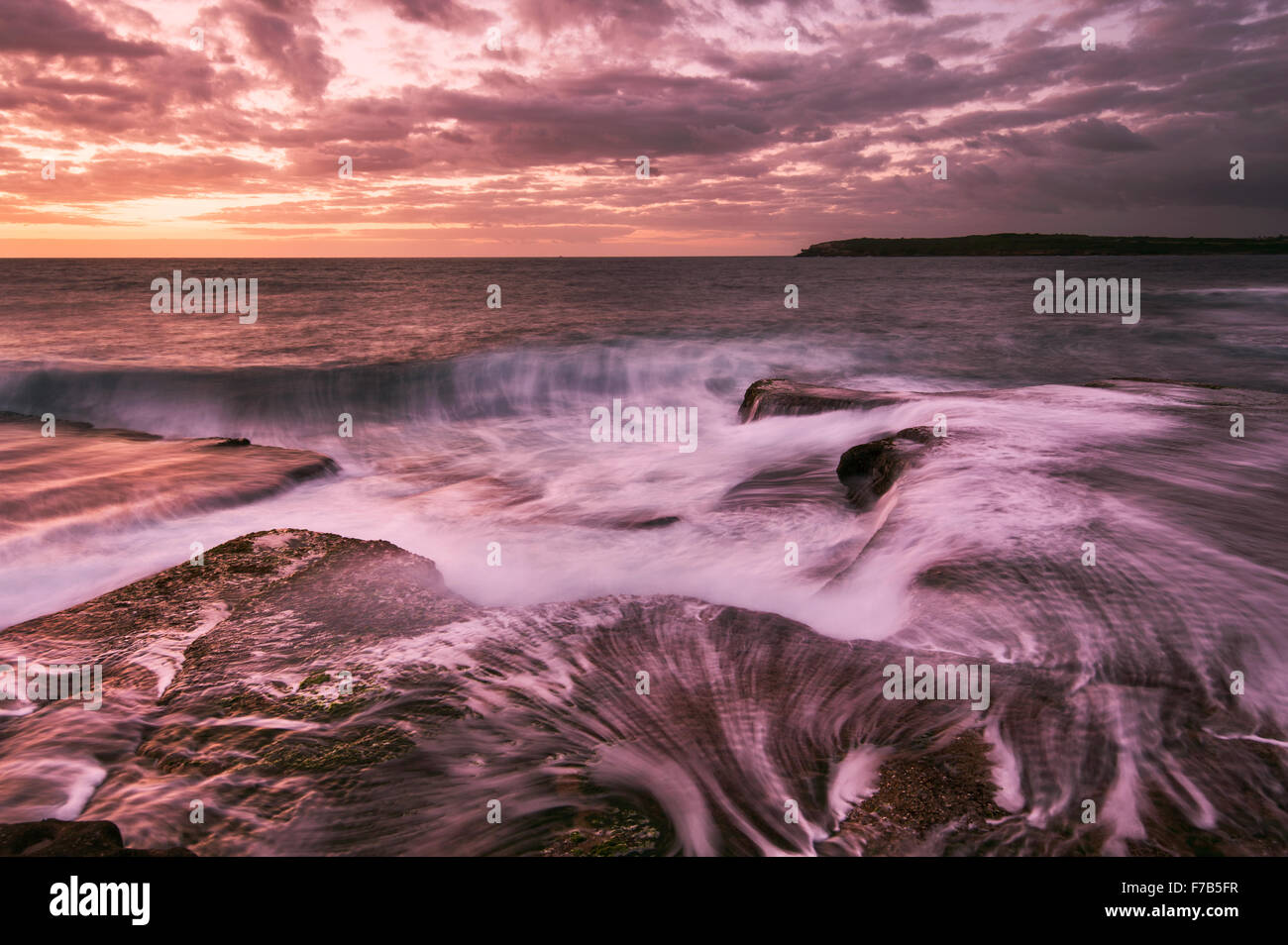 Sunrise seascape water with waves and small rocks waterfall in magenta tones in Sydney Australia Stock Photo