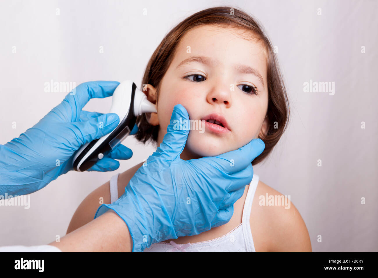 Doctor measuring temperature weak little girl with ear talking electronic thermometer. Isolated over white background Stock Photo