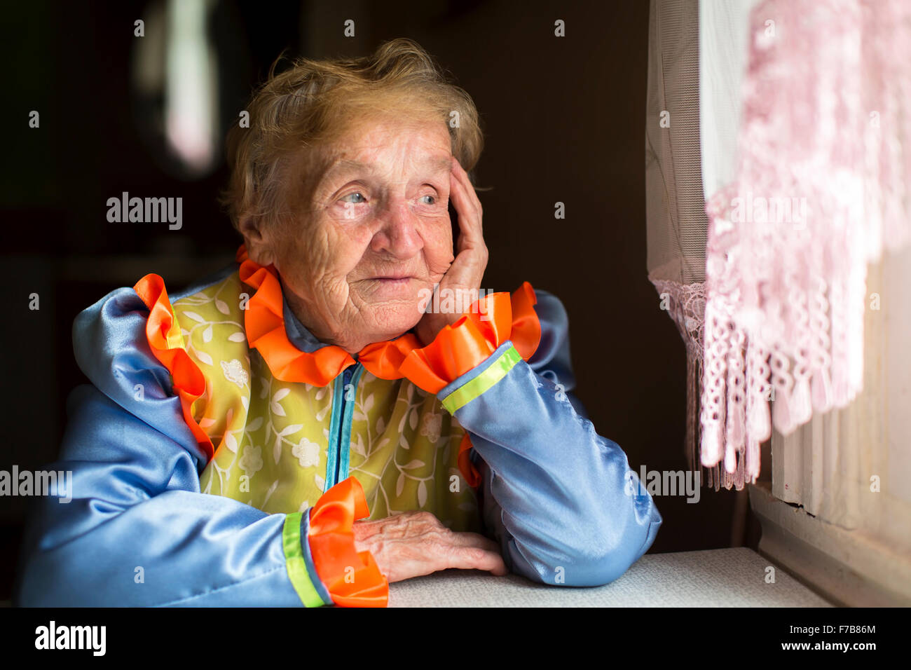 Elderly woman sadly looking out the window. Stock Photo