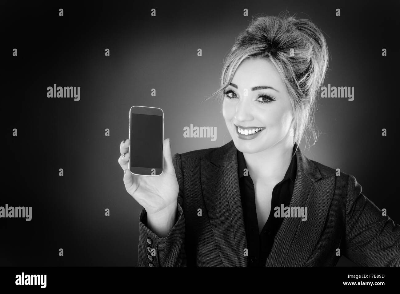 business woman holding up a mobile phone and showing you the screen shot in the studio on a gray background. Stock Photo