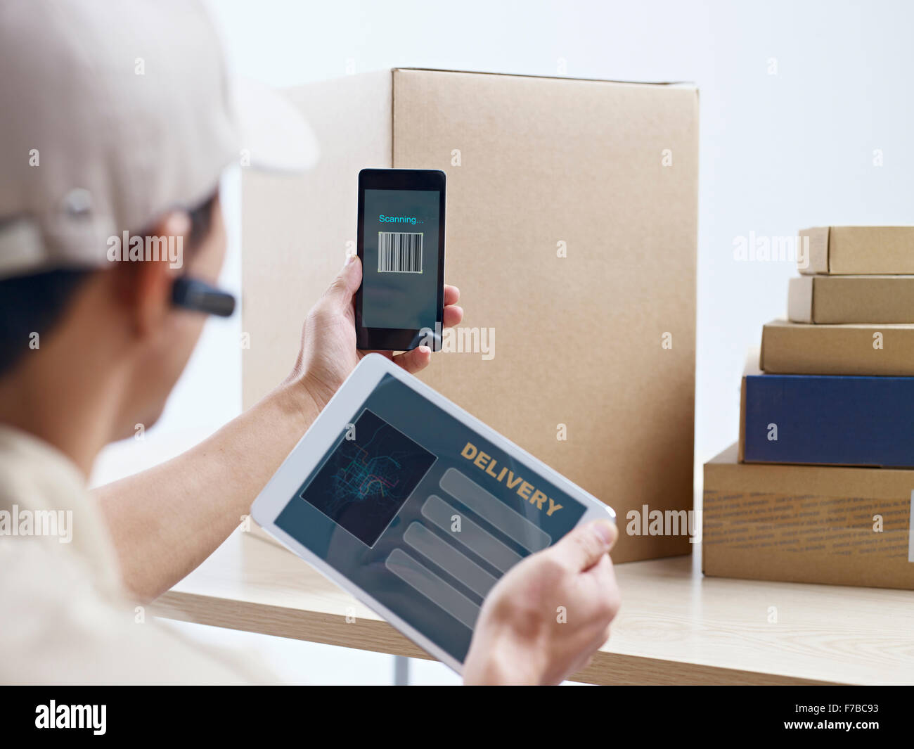 male asian courier company worker using cellphone and tablet computer to scan information on packages. Stock Photo