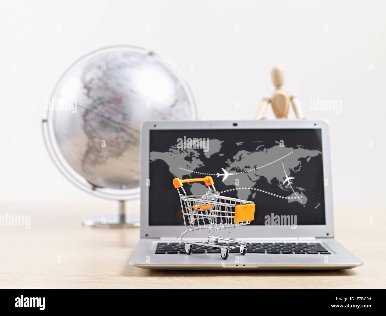toy shopping cart on top of laptop computer with wooden dummy and world globe in background. Stock Photo