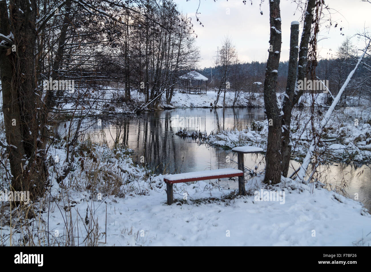 Winter landscape in park with small bench and river with reflection ...
