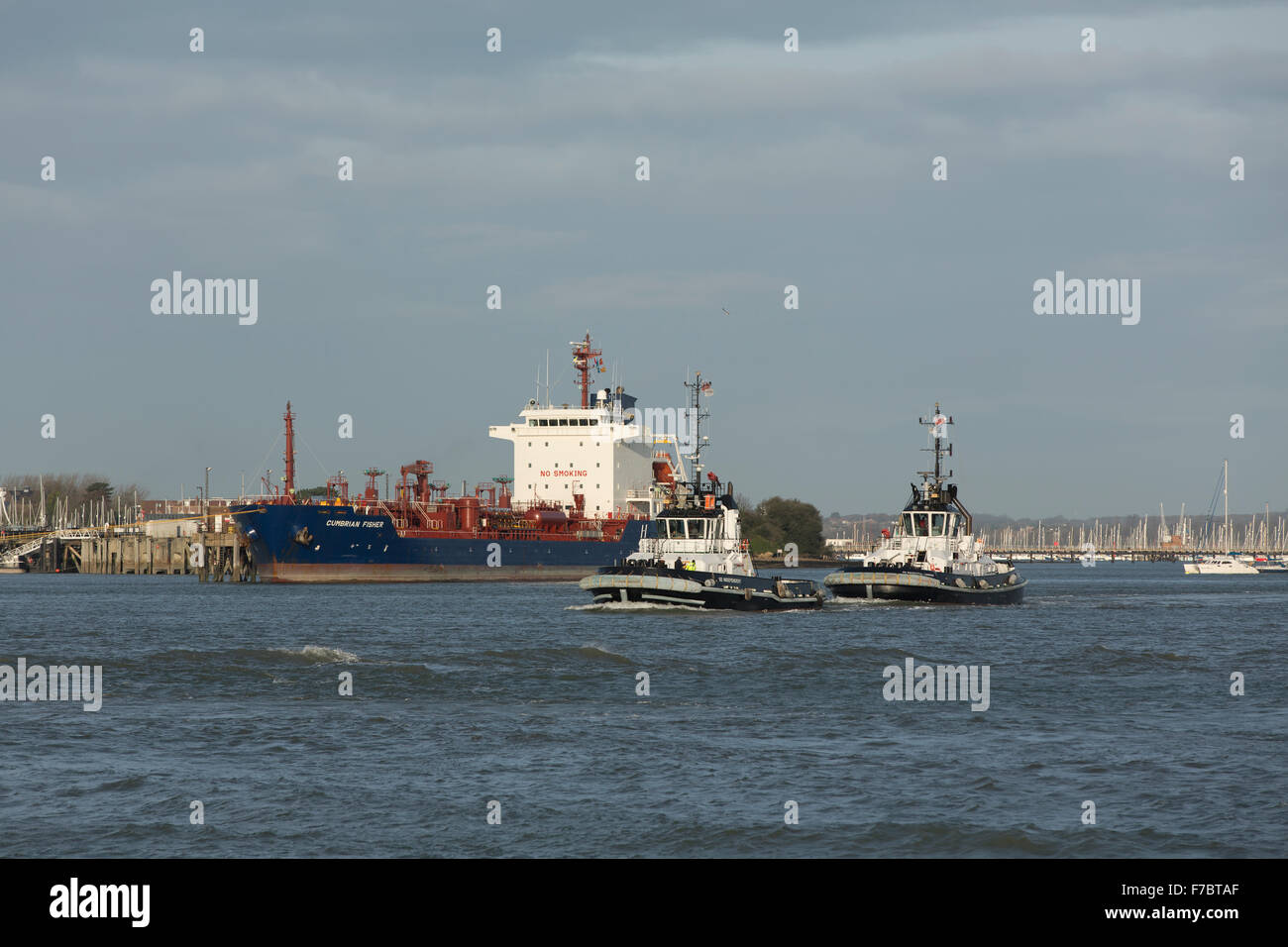 Matching tug boats heading out of Portsmouth harbour. White and black work boats preparing for the arrival of a container ship. Stock Photo