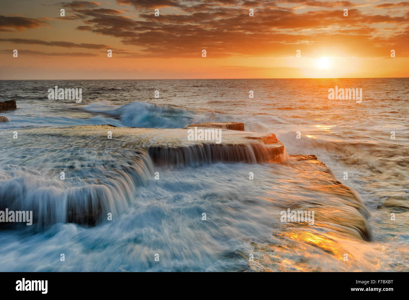 Pacific ocean scenic colourful sunrise over horizon near Maroubra beach in Sydney with falling sufring water from coastal rocks Stock Photo