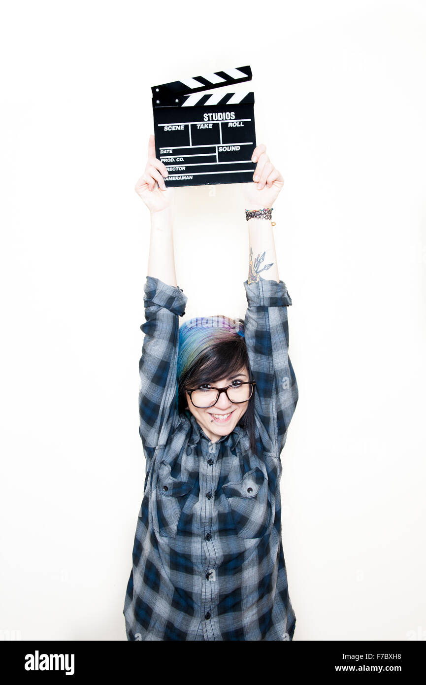 Pretty young alternative teen woman smiling and holding movie clapper on head Stock Photo
