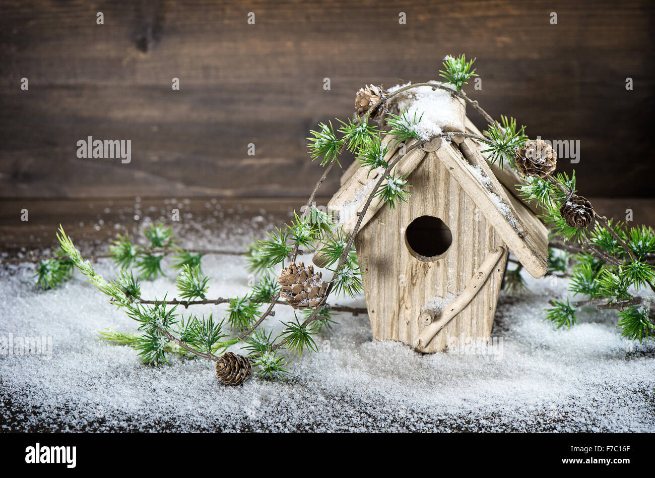Birdhouse and christmas tree brunch decoration in snow over rustic wooden background. Stock Photo