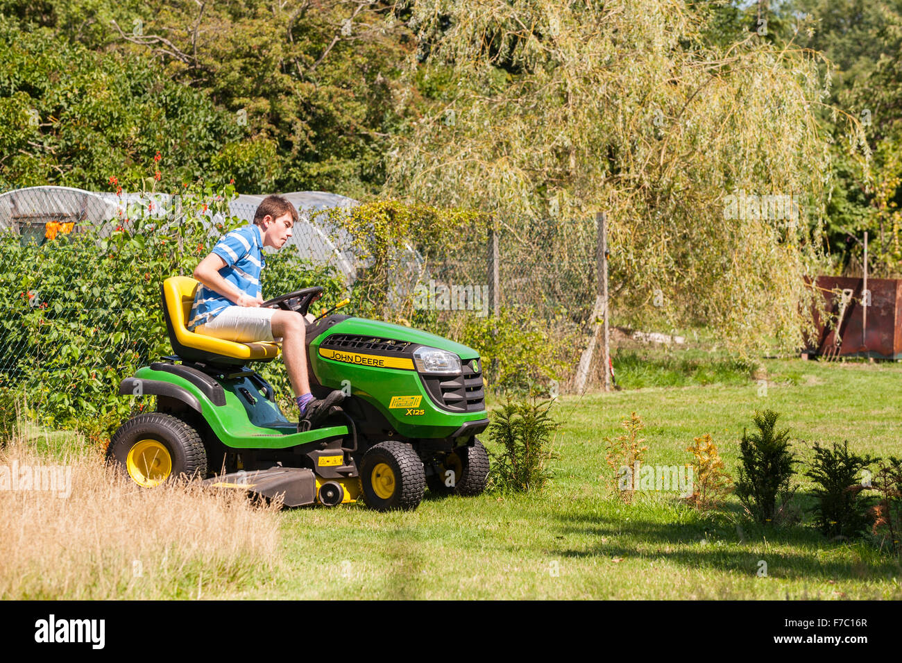 A 15 year old boy mowing the lawn on a John Deere ride on mower in the Uk Stock Photo