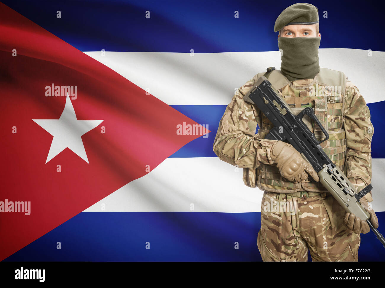Soldier holding machine gun with national flag on background - Cuba Stock Photo