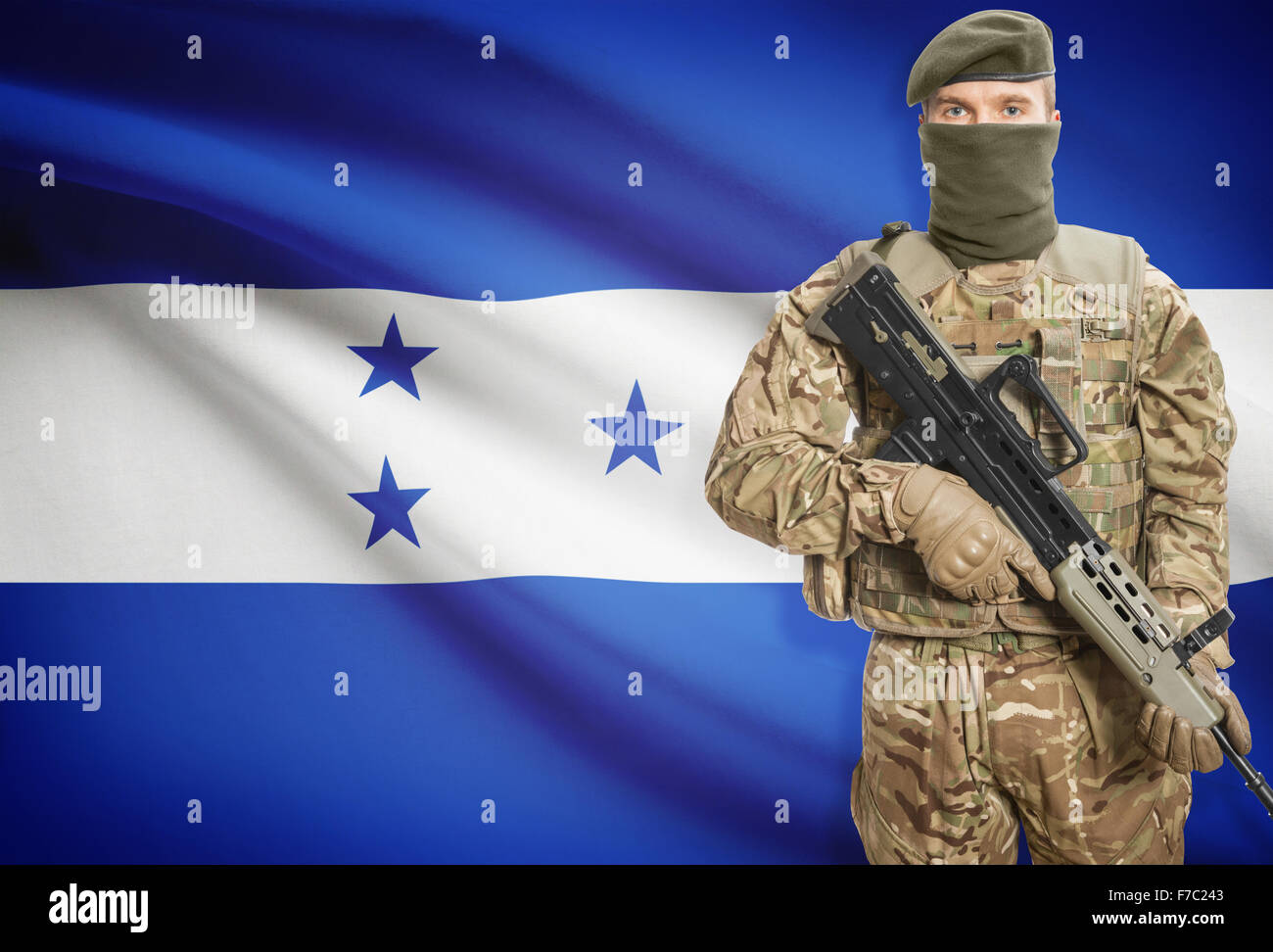 Soldier holding machine gun with national flag on background - Honduras Stock Photo