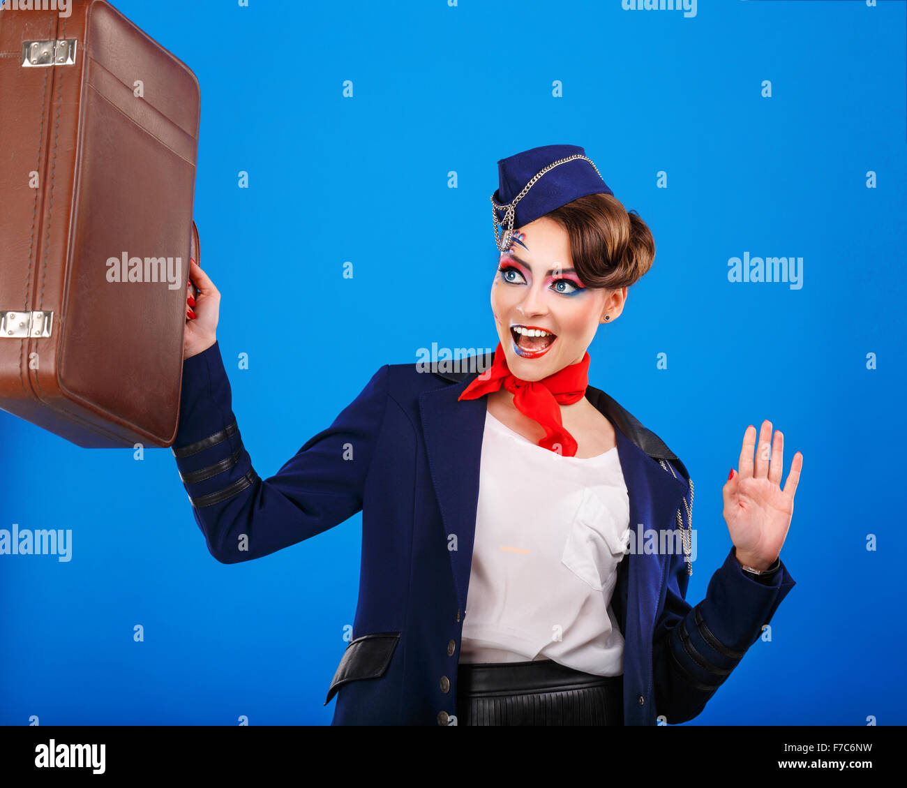 Stewardess with face art holds suitcase. Young attractive girl in a blue suit flight attendants. Air transportation. Service. Stock Photo